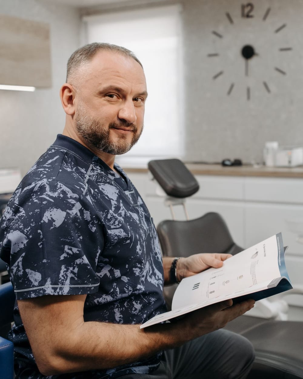 A dentist seated in a treatment room reading a printed report