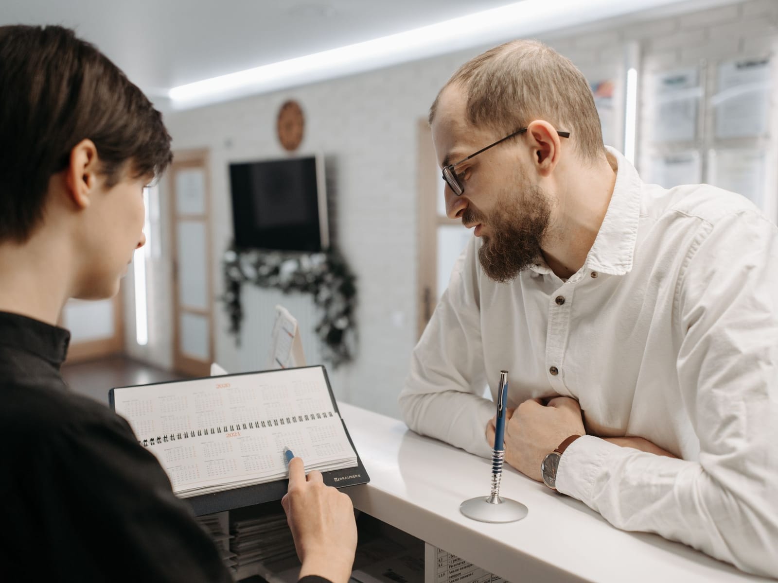 A receptionist showing an appointment calendar to a patient at a dental practice front desk