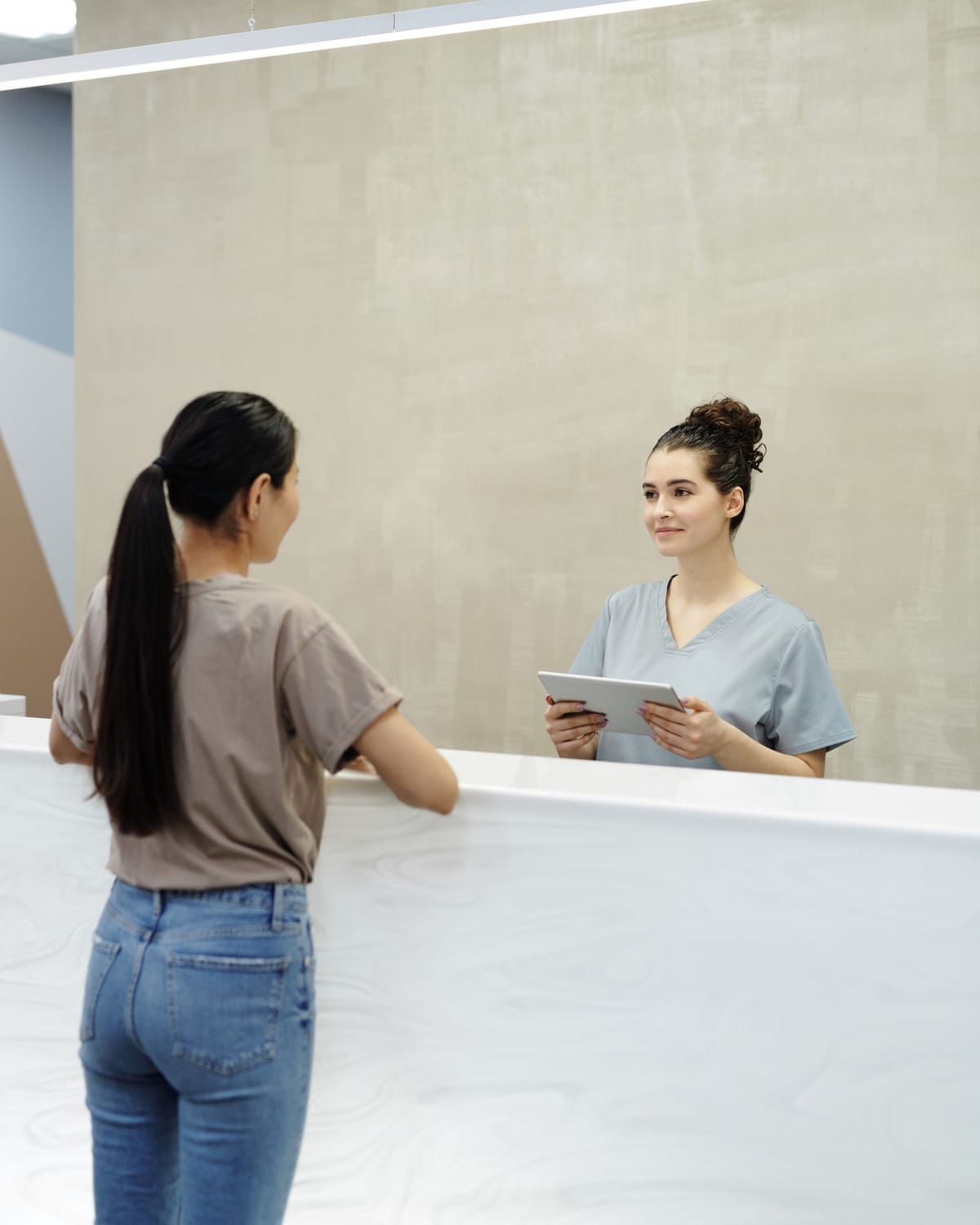 A patient talking to a receptionist holding a tablet at a clinic front desk